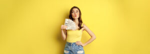 woman holding money against a plain yellow background